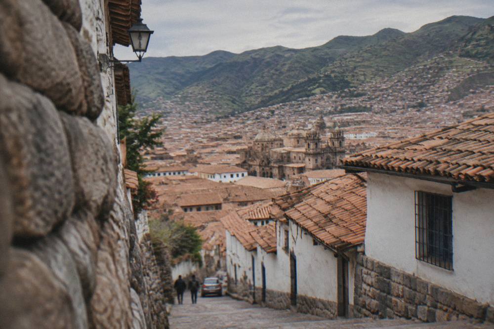 Terracotta rooftops of Cusco spreading across a hillside with green mountains behind