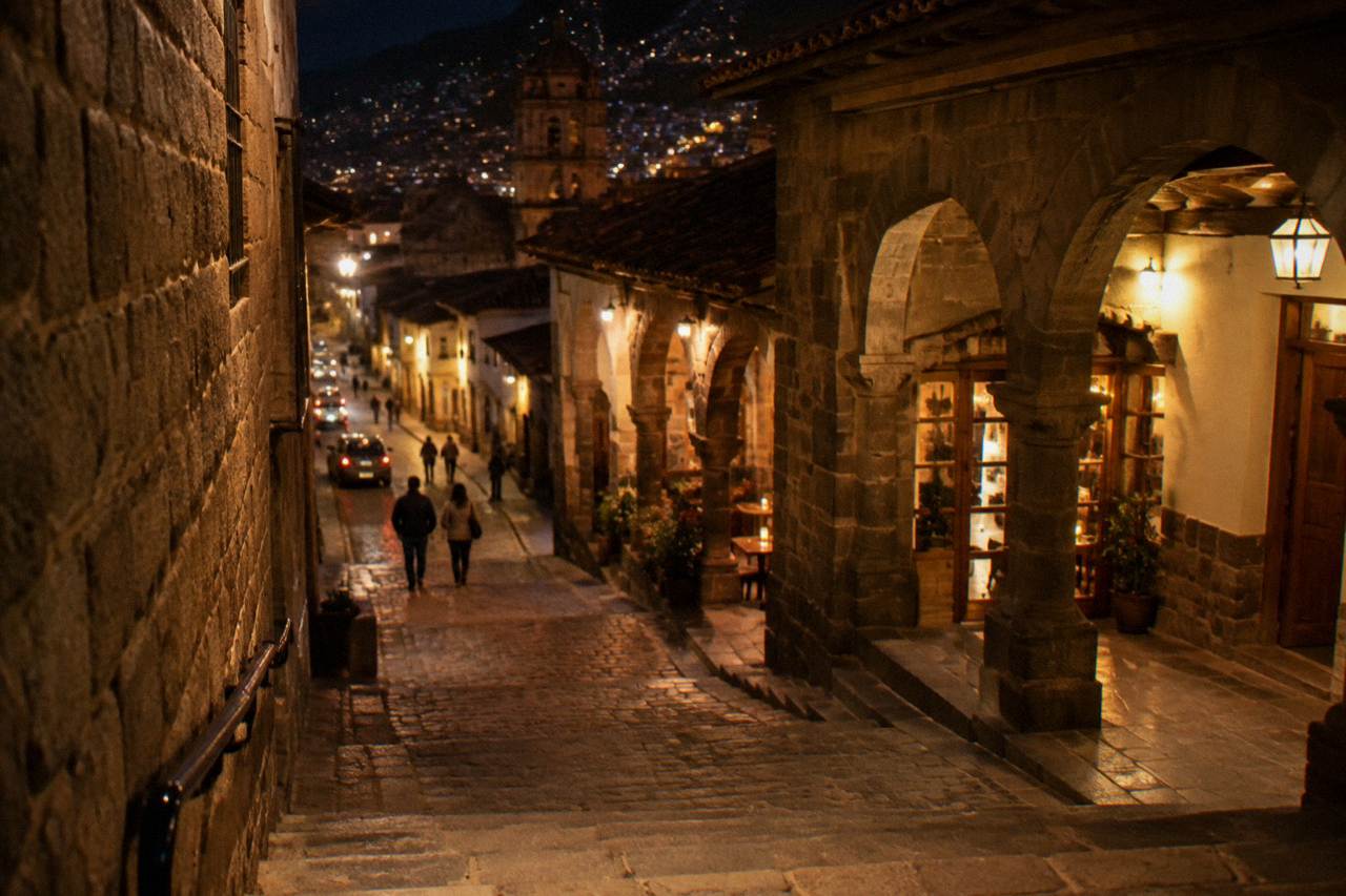 An evening street in Cusco's historic centre with lit restaurant doorways and stone walls