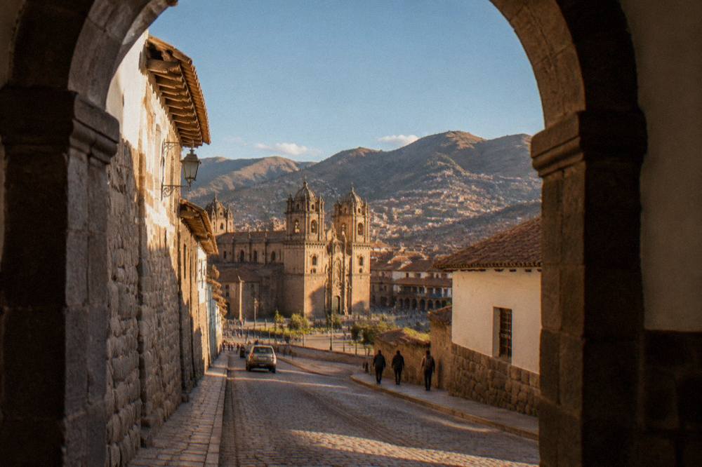 A narrow colonial street in Cusco with stone walls under a clear blue sky