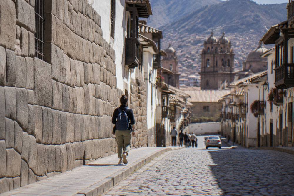 A quiet colonial street in central Cusco with stone walls and a visitor walking slowly uphill