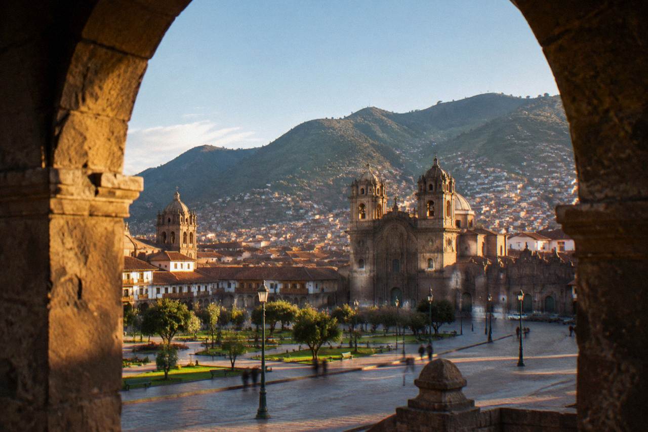 Red tiled roofs and colonial church towers of Cusco under morning light with green hills rising behind the city
