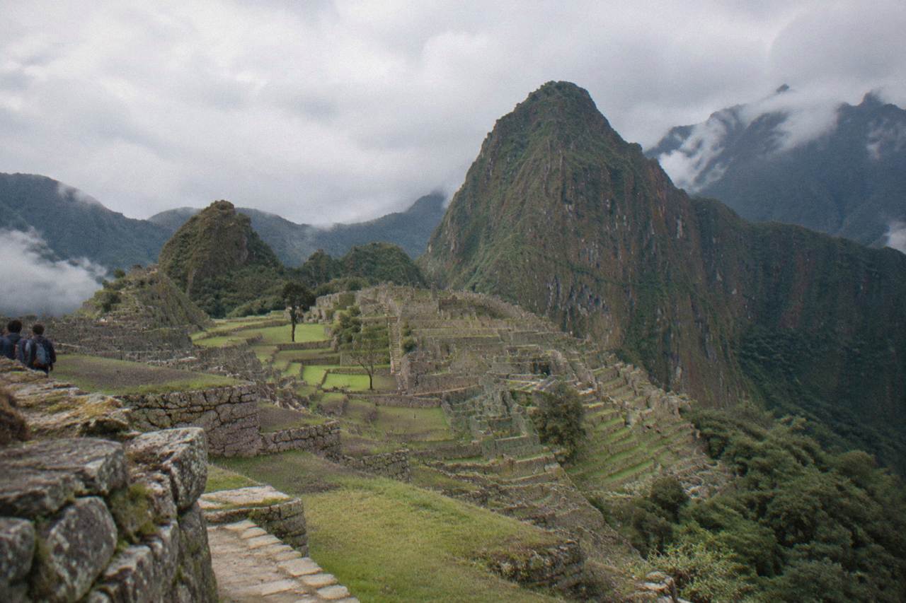 The stone terraces and ruins of Machu Picchu on a green mountainside under a cloudy sky