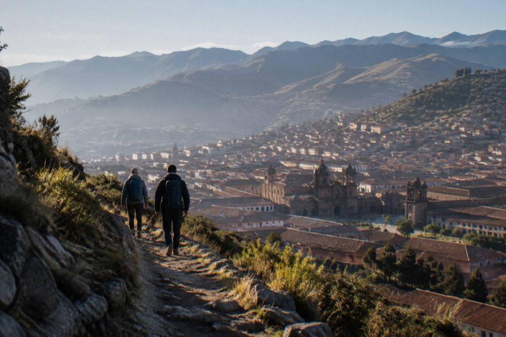 Two hikers with backpacks walking a high Andean trail above Cusco in morning light