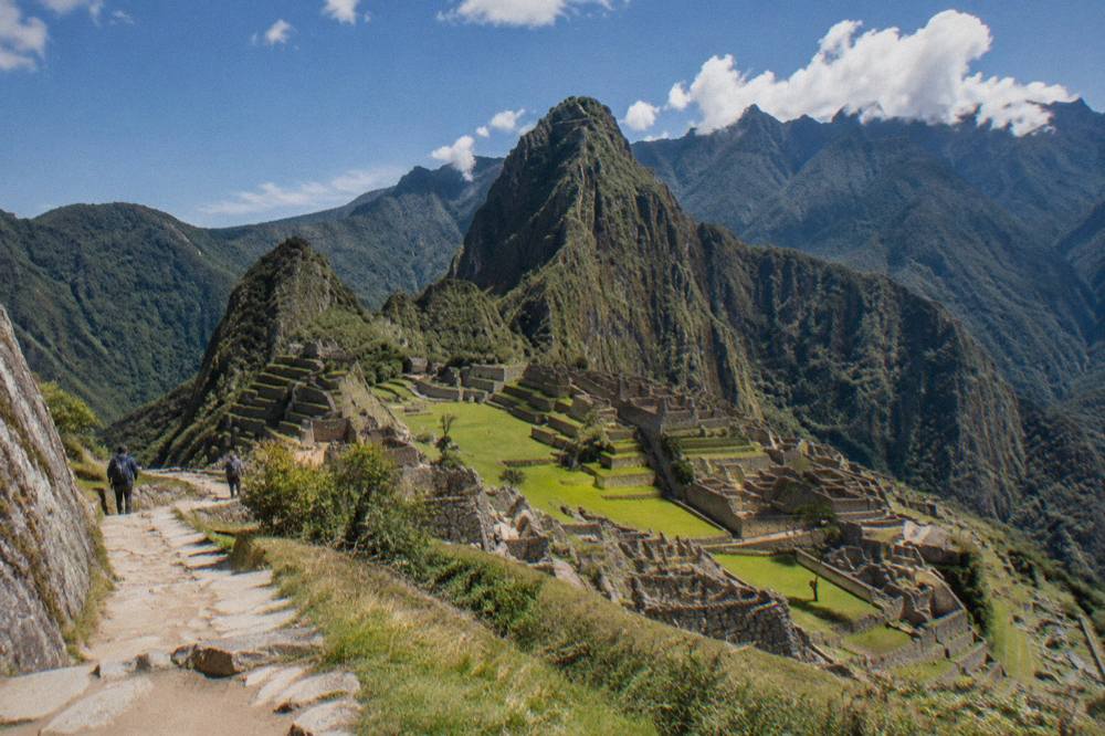 Stone terraces of Machu Picchu on a green ridge with forested mountains behind