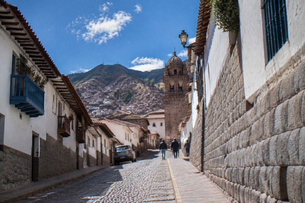 A narrow cobblestone street of stone-walled buildings climbing a hillside in Cusco's historic centre