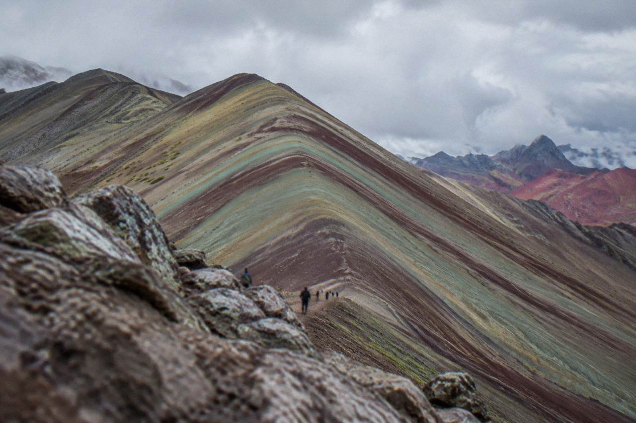 Striped bands of red, gold and turquoise mineral layers on a high Andean mountain ridge under a wide sky