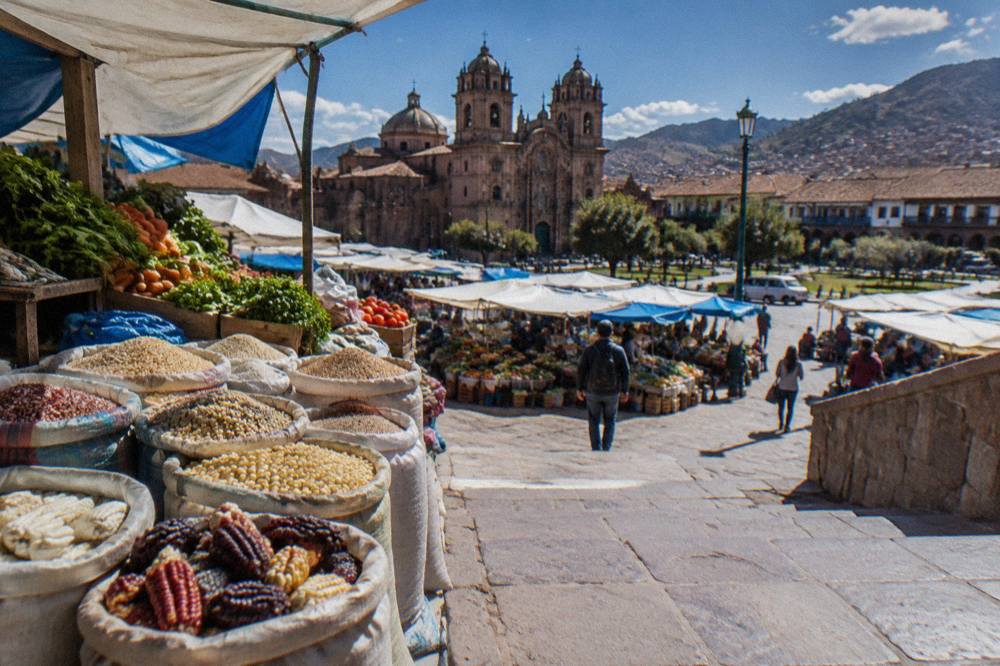Fresh produce and grain stalls at a Cusco market with sacks of corn and quinoa