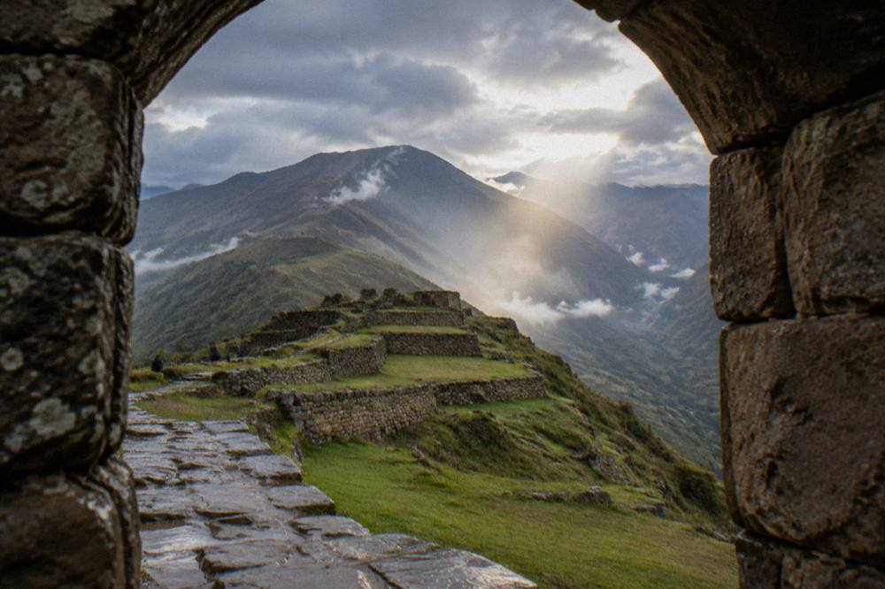 Terraced stone ruins on a green mountain ridge with morning mist in a high valley