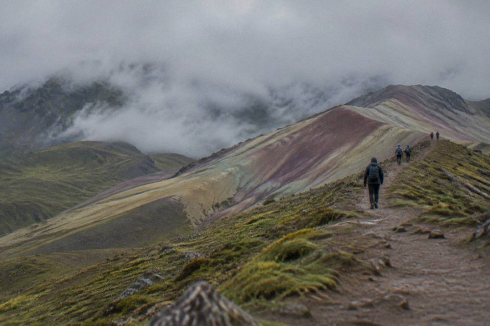 Walkers on a dirt path climbing towards a ridge with coloured mineral slopes