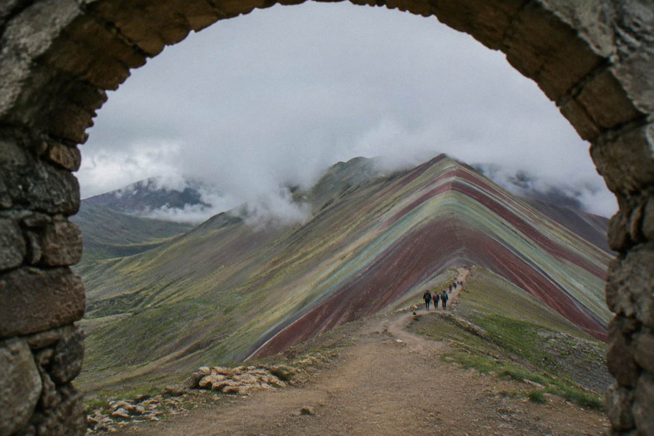 Striped mineral slopes of a high Andean mountain under a wide sky with a dirt path leading toward the ridge