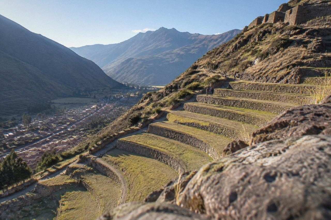 Terraced Inca agricultural terraces on a hillside above a valley town in the Peruvian Andes under a clear sky