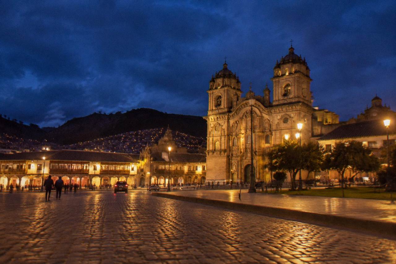 Cusco Plaza de Armas lit up at night with the cathedral illuminated and the surrounding colonial arcades