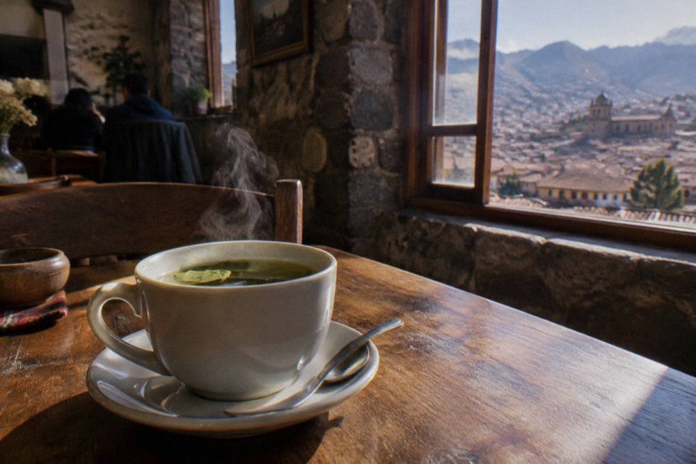 A steaming cup of coca tea on a cafe table in a stone-walled room in Cusco
