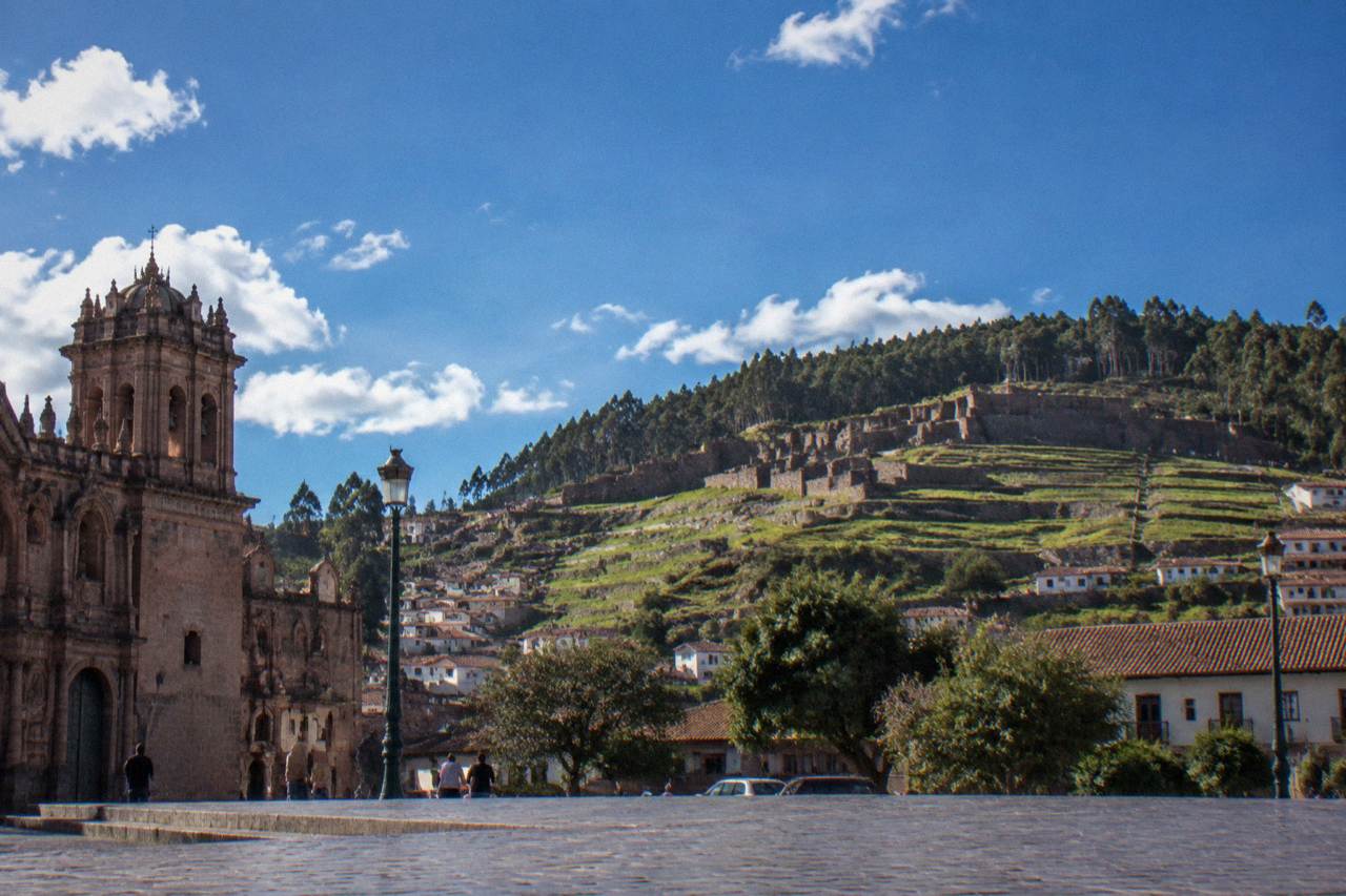 Stone Inca walls and colonial arcades around a plaza in the Peruvian Andes under a wide blue sky