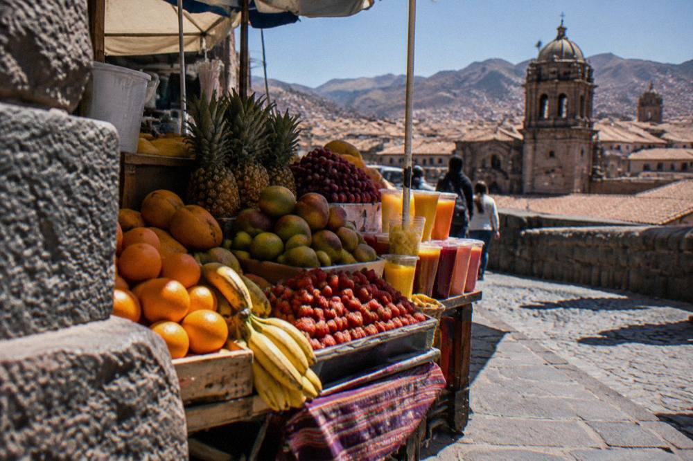 A busy market stall in Cusco stacked with fresh fruit and glasses of juice
