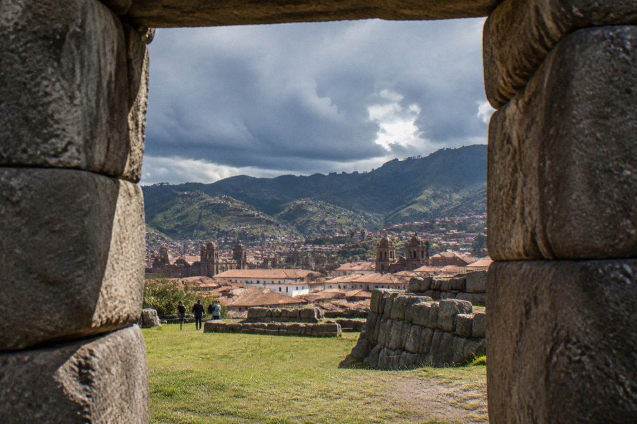 Rain clouds gathering over the red tiled roofs and church towers of Cusco with green hills behind