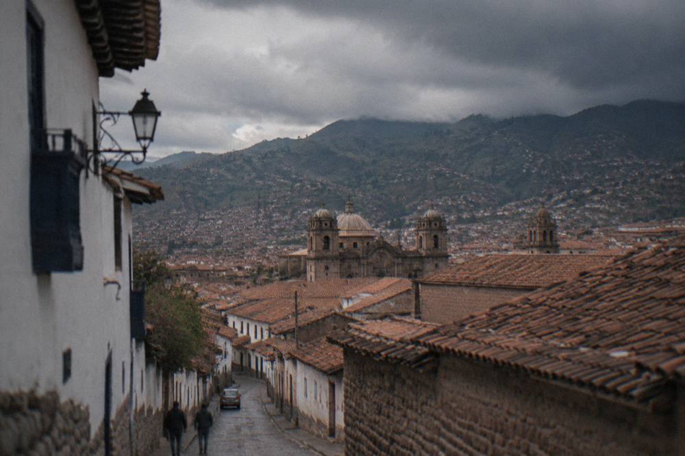 Rain clouds gathering over terracotta rooftops of Cusco with green hills behind