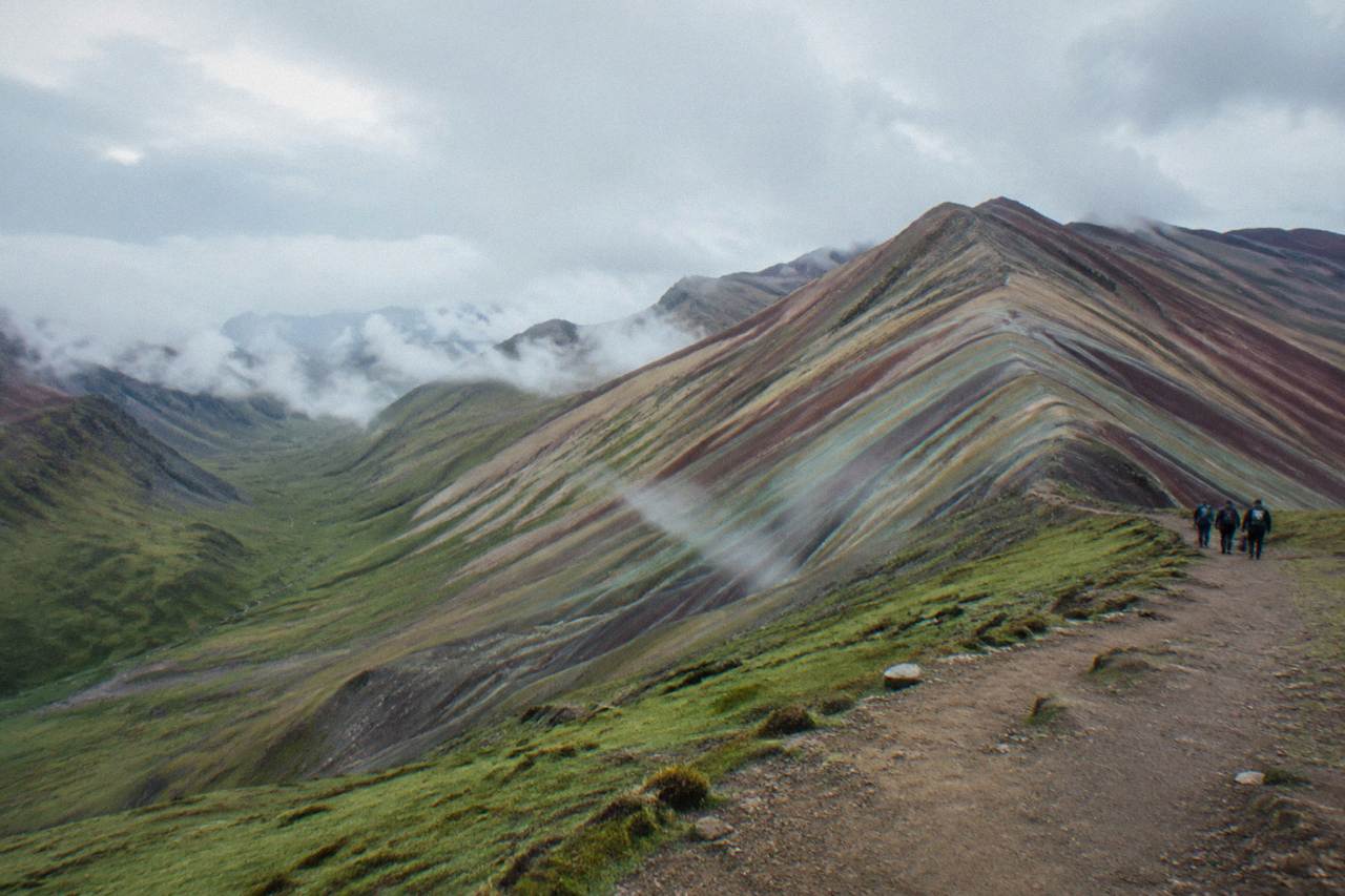 Striped ridges of a high Andean mountain under a wide sky with a dirt trail along the slope