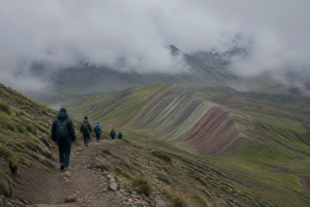 A group of walkers in warm coats descending a high ridge trail with striped slopes below