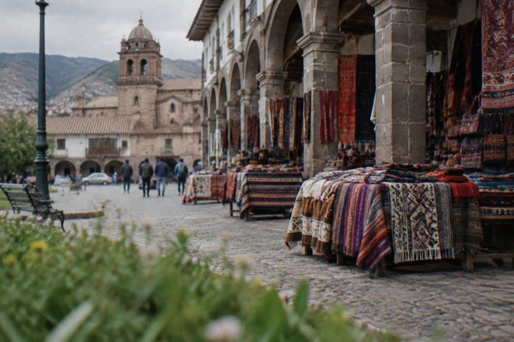 Open-air craft market with woven textiles spread under stone arcades