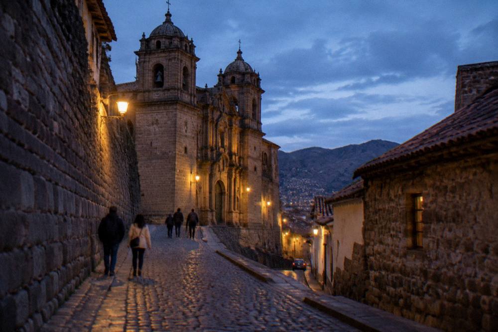 Pedestrians climbing a steep cobbled lane between old stone walls in an Andean town