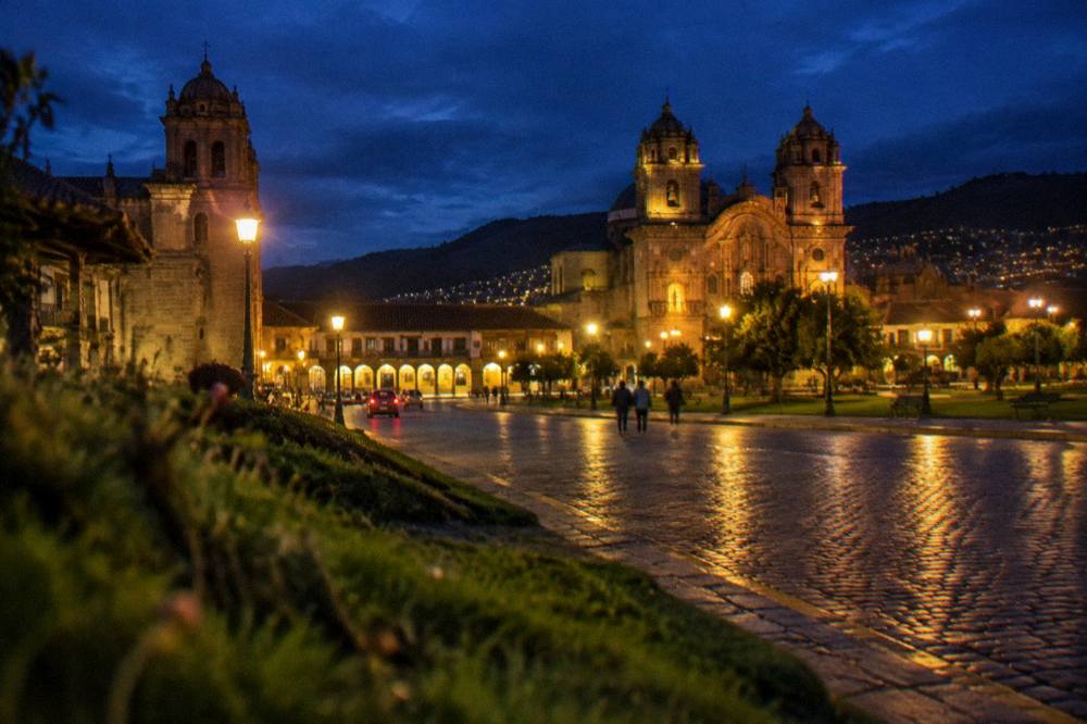 Illuminated stone plaza at night with lit church towers above the rooftops