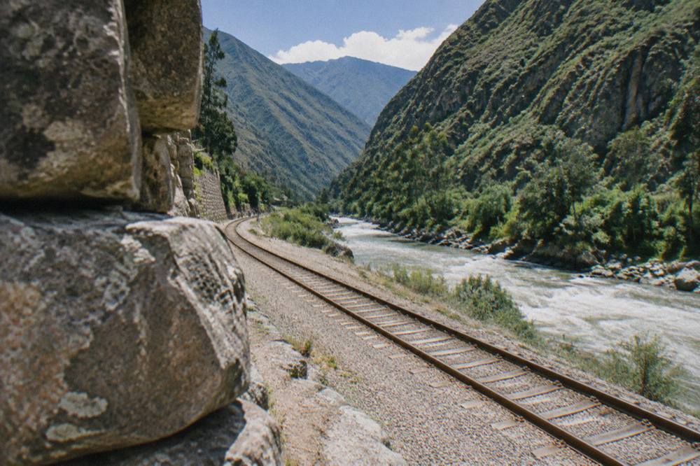 Train tracks running Along A River Between Green Mountains In The Valley