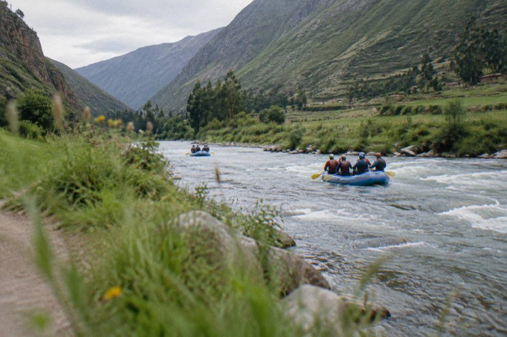 Inflatable rafts on a river flowing past green valley slopes