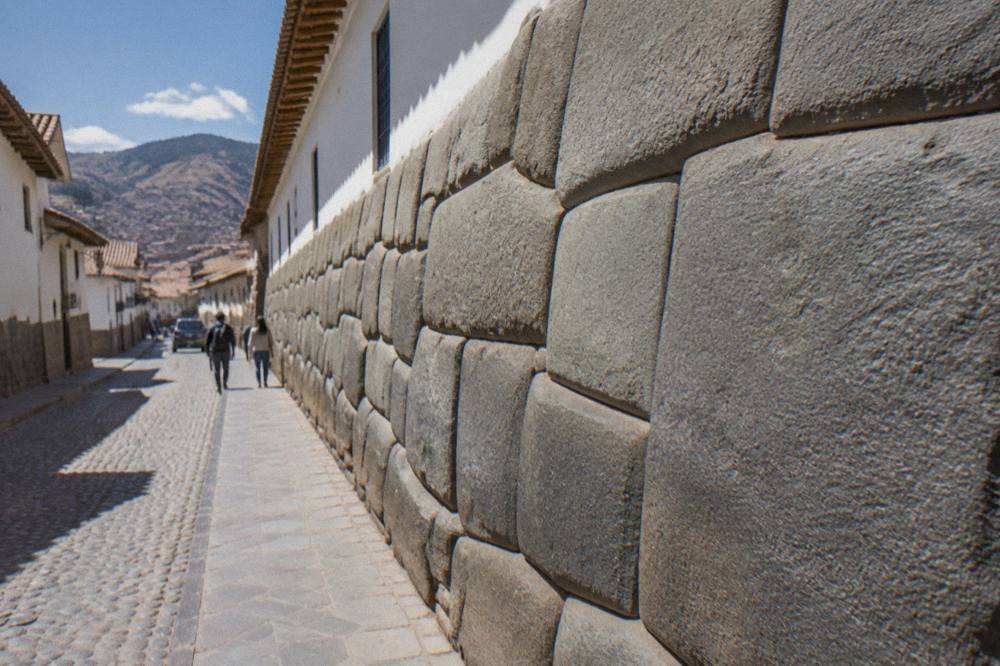 A stone staircase lane between colonial walls rising toward a church tower in Cusco