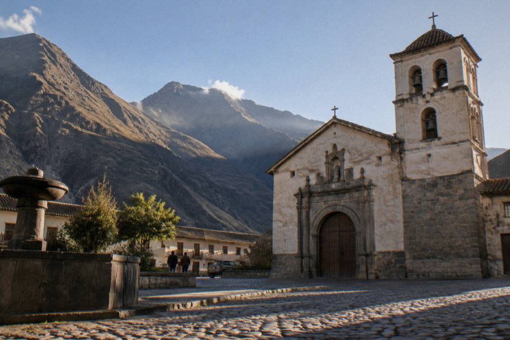 A small plaza with a church facade and mountains in the background