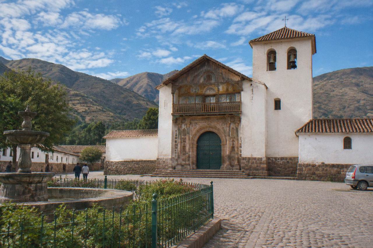 A small Andean village square with a white colonial church facade under a bright blue sky