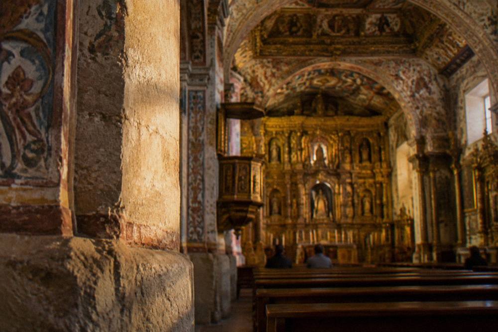 A painted church interior with gilded altar and ceiling decoration seen from the nave
