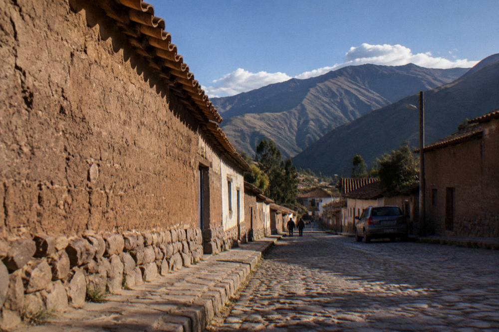 A quiet Andean village street with adobe walls and mountains beyond in late afternoon