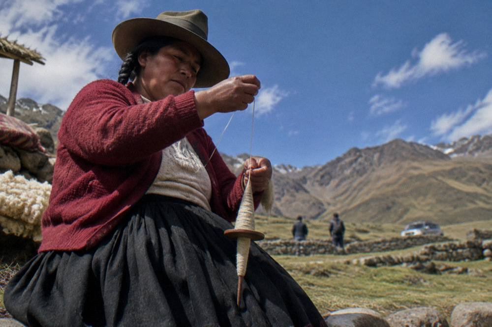 A woman in traditional Andean dress spinning yarn with a drop spindle