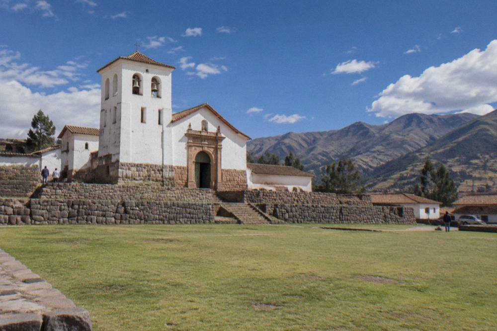 A colonial church standing on Inca stone walls above a grassy plaza in Chinchero