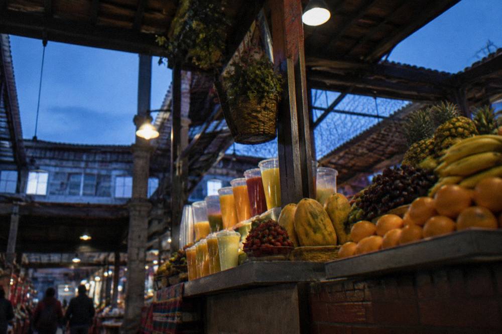 A vendor displaying fruit juices and produce inside a covered market hall