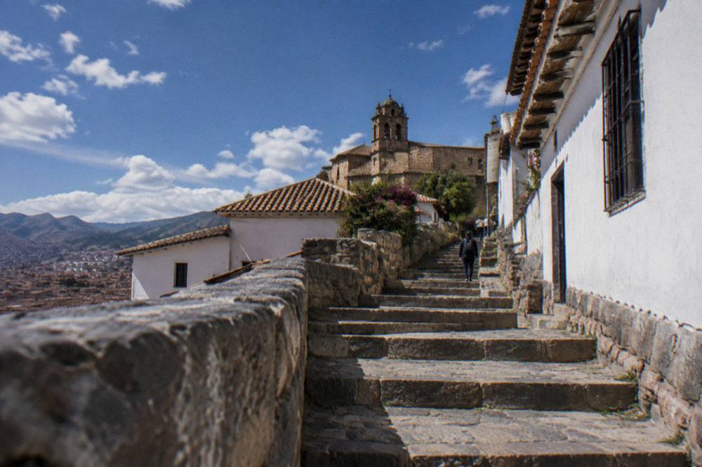A steep stone stairway climbing between whitewalled houses on a hillside in Cusco