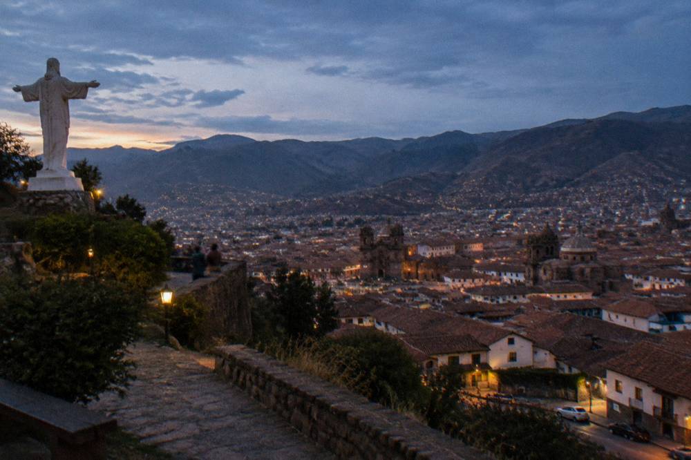 A panorama of red rooftops, church domes and mountain ridges seen from a high hillside terrace