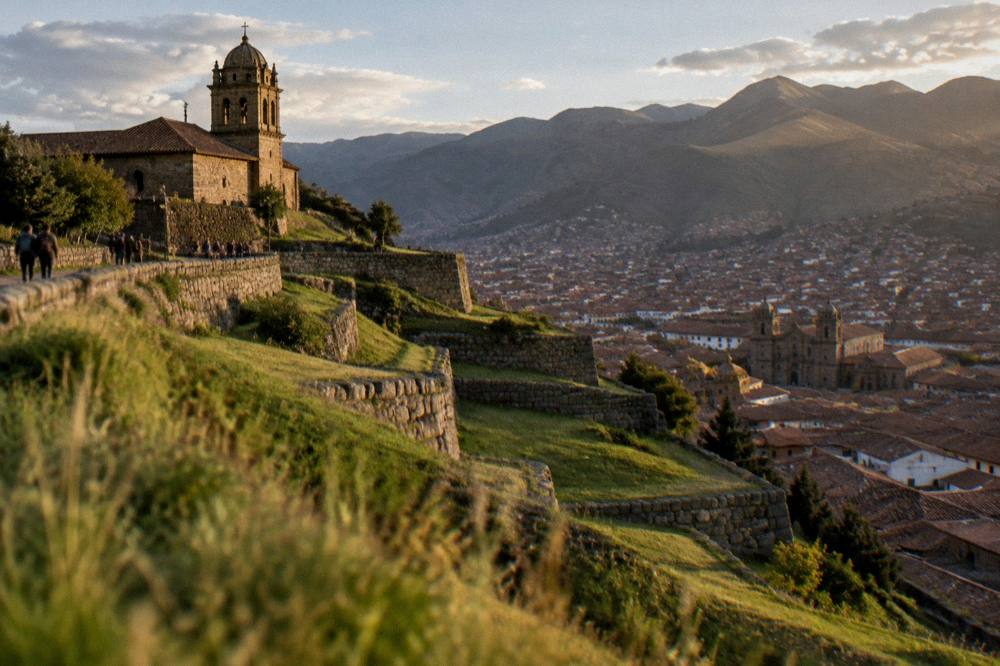 Long terraced stone walls on a high grassy hillside above a city