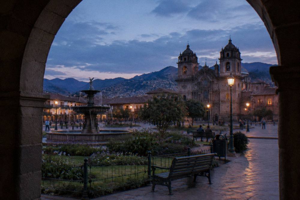 Wide view across the Plaza de Armas with the Cathedral facade and arcades under a clear sky