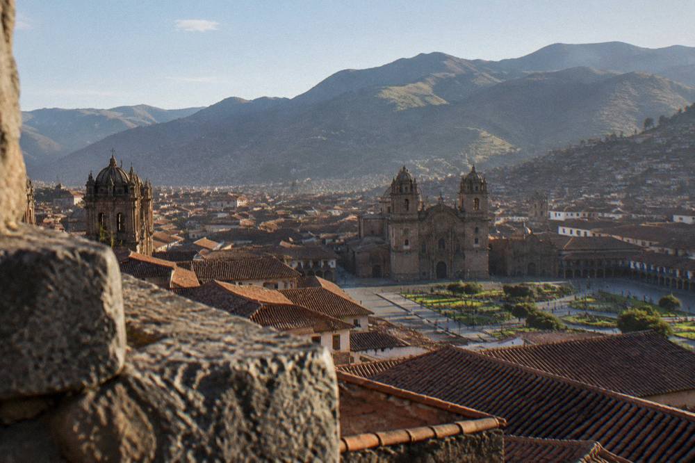 View over the red rooftops of Cusco toward the Plaza de Armas and the Cathedral towers from the hills above