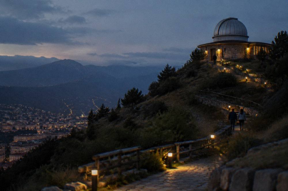 A lit path leading up to a small observatory building on a hillside at dusk