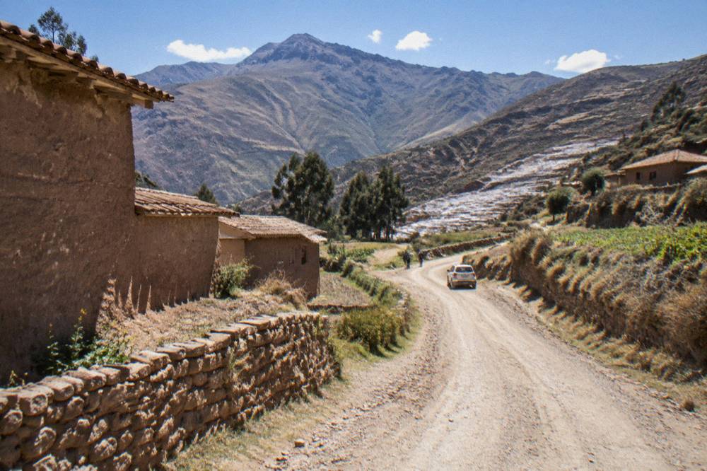 Rural road winding between adobe houses and fields on the way to the Maras salt pans