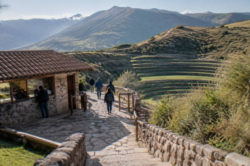 A ticket window and stone entrance path at an Andean archaeological site with visitors walking in