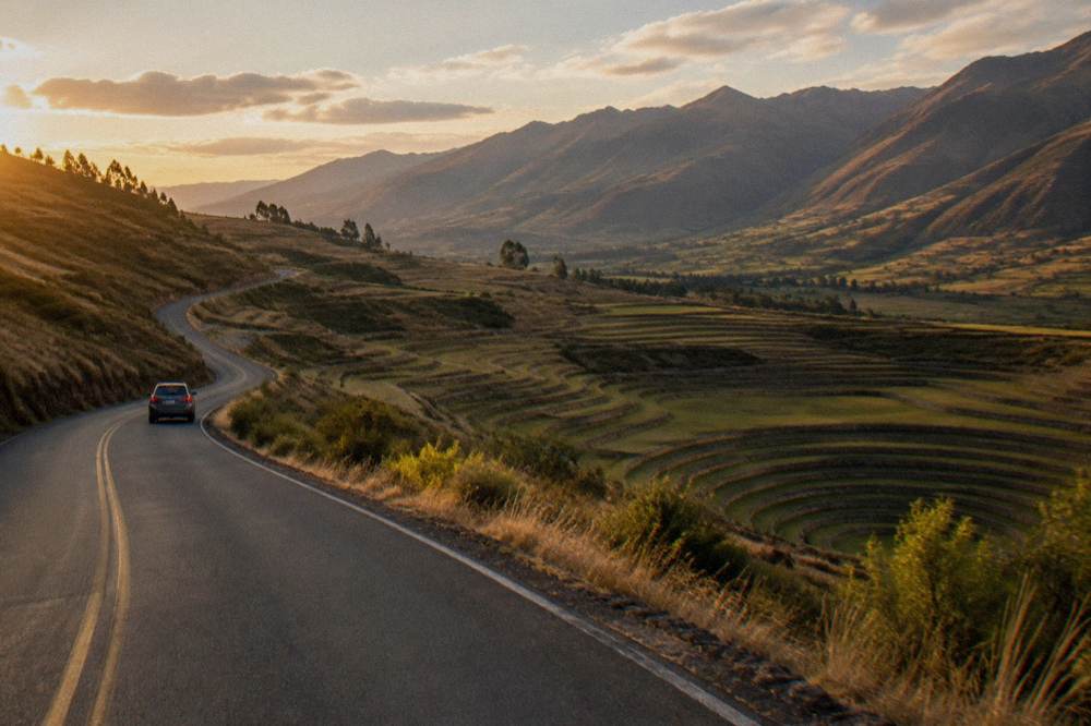 A winding asphalt road across high grassland toward terraced hills in the Sacred Valley