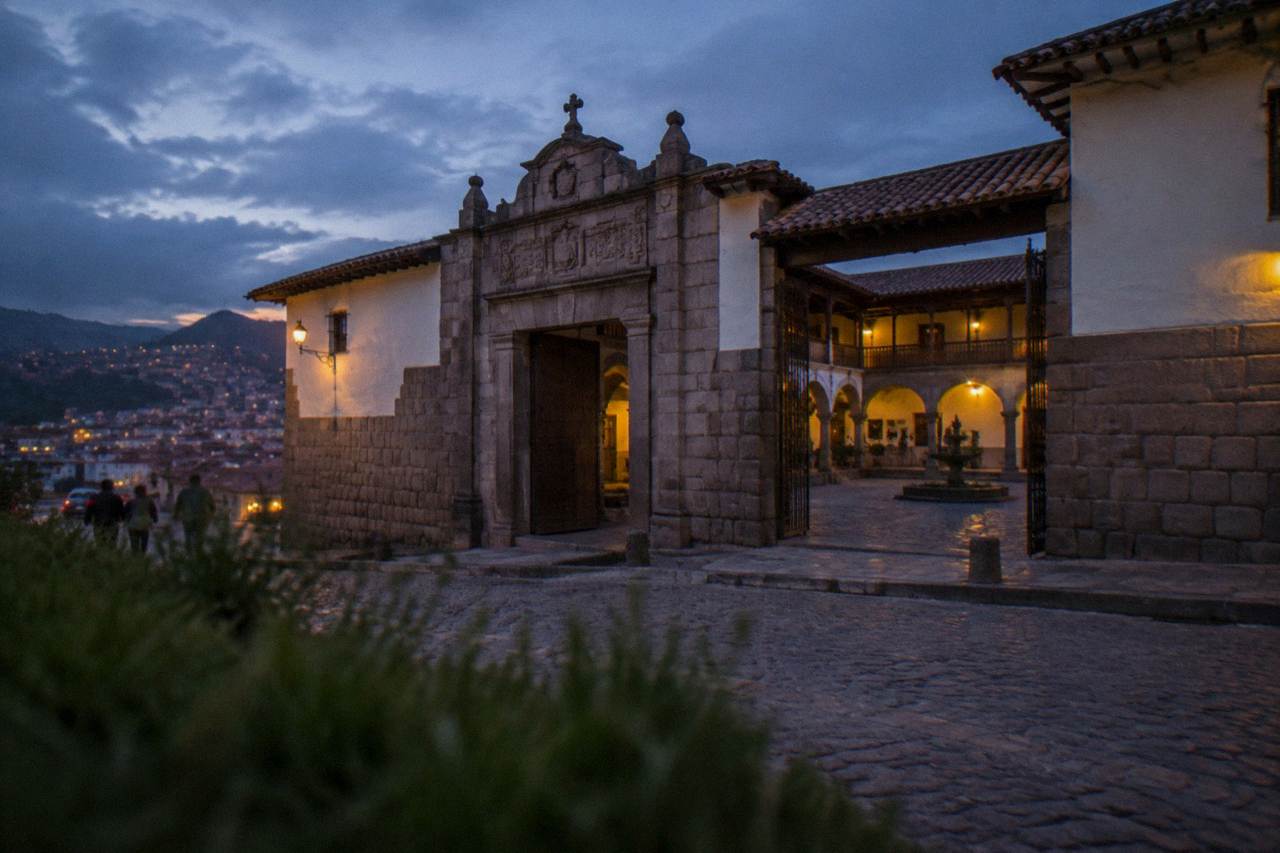 A colonial stone arcade in central Cusco with a museum entrance and visitors reading a display panel