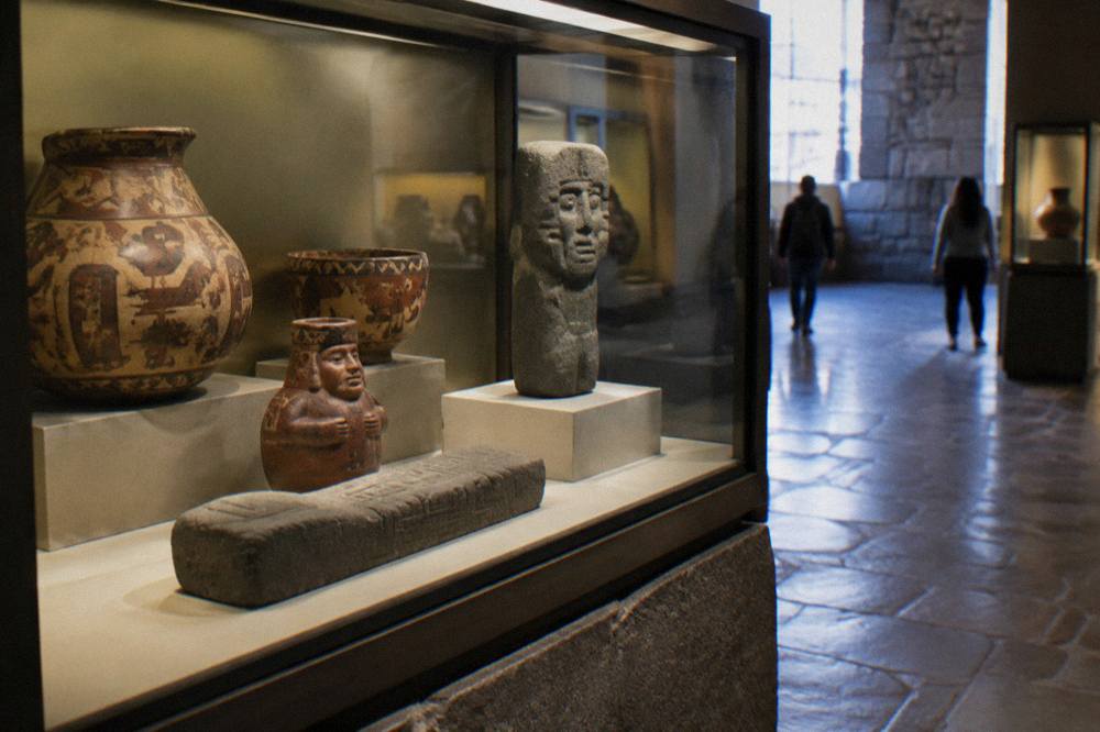 A display case of Inca pottery and stone objects lit inside a museum gallery