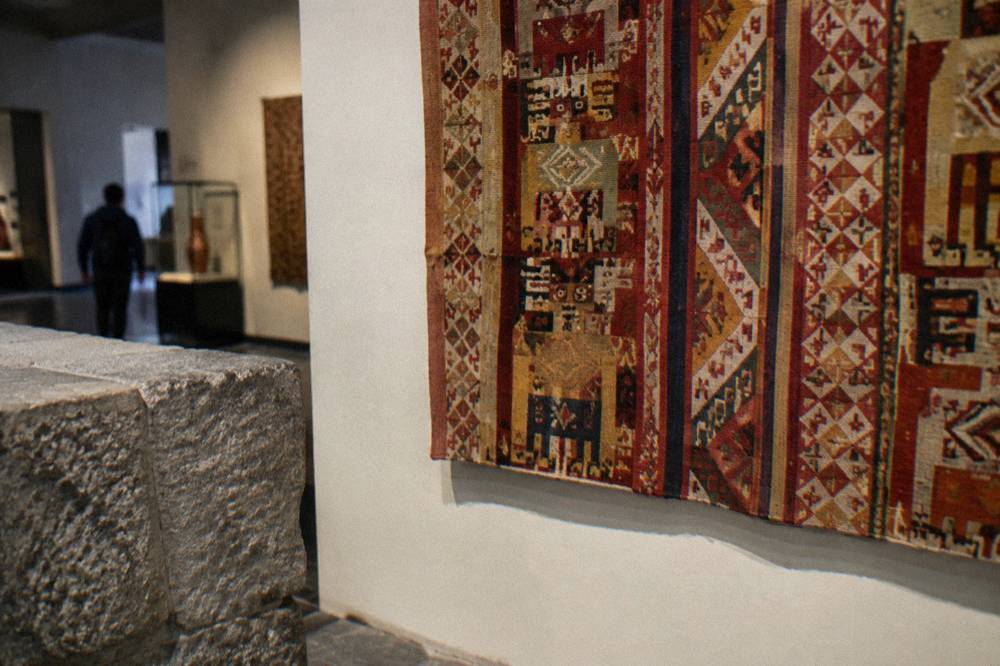 A woven textile with Andean patterns displayed on a museum wall