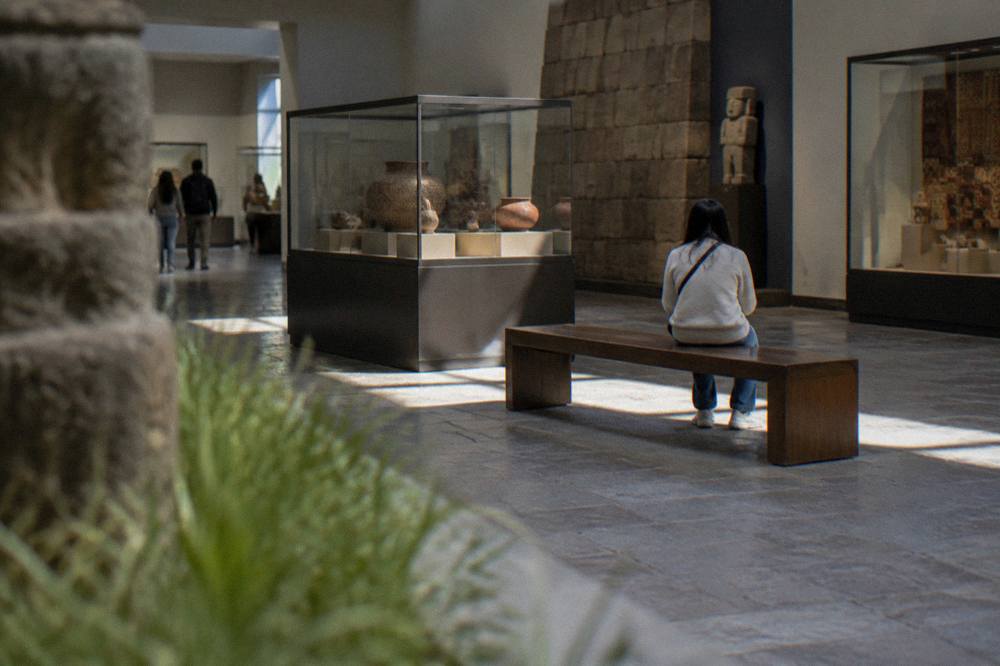 A quiet indoor gallery with a visitor resting on a bench beside display cases
