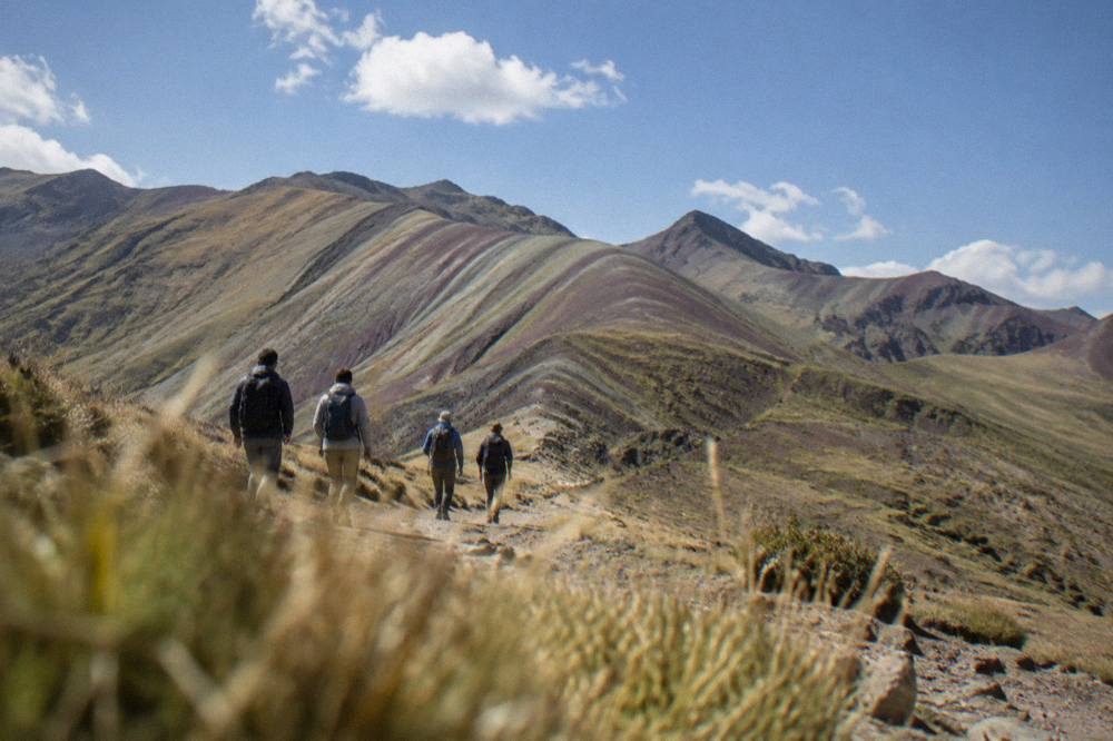 A group of visitors on a high Andean trail with striped mountain slopes in the distance